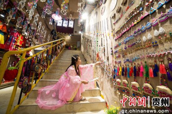 7月4日，在贵州省毕节市大方县奢香古镇聚民艺彝族文化服饰店，龙恩碧正在帮顾客挑选服装。