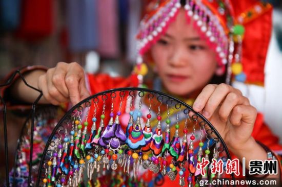 7月4日，在贵州省毕节市大方县奢香古镇聚民艺彝族文化服饰店，龙恩碧正在帮顾客挑选服装。